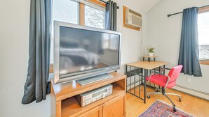 Una sala de estar moderna con un televisor de pantalla plana sobre un mueble de madera, una mesita con una silla y una planta en maceta.