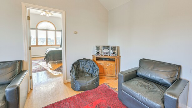 Un salón con alfombra roja, dos sofás de cuero, un sillón de mikasa, un mueble de madera con altavoces y una puerta que da a otra habitación.