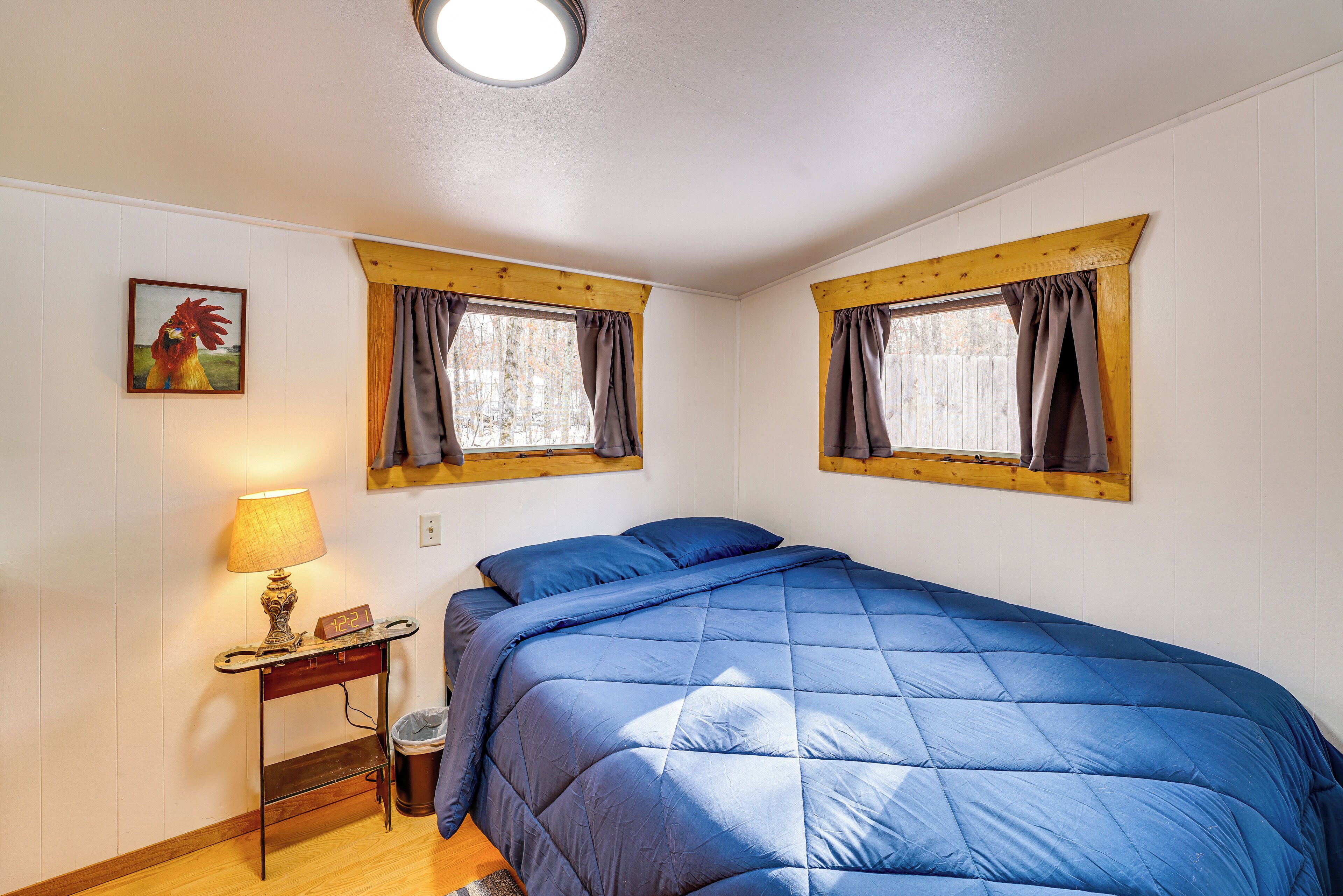 A bedroom with a bed, a nightstand, a lamp, and two windows with curtains.