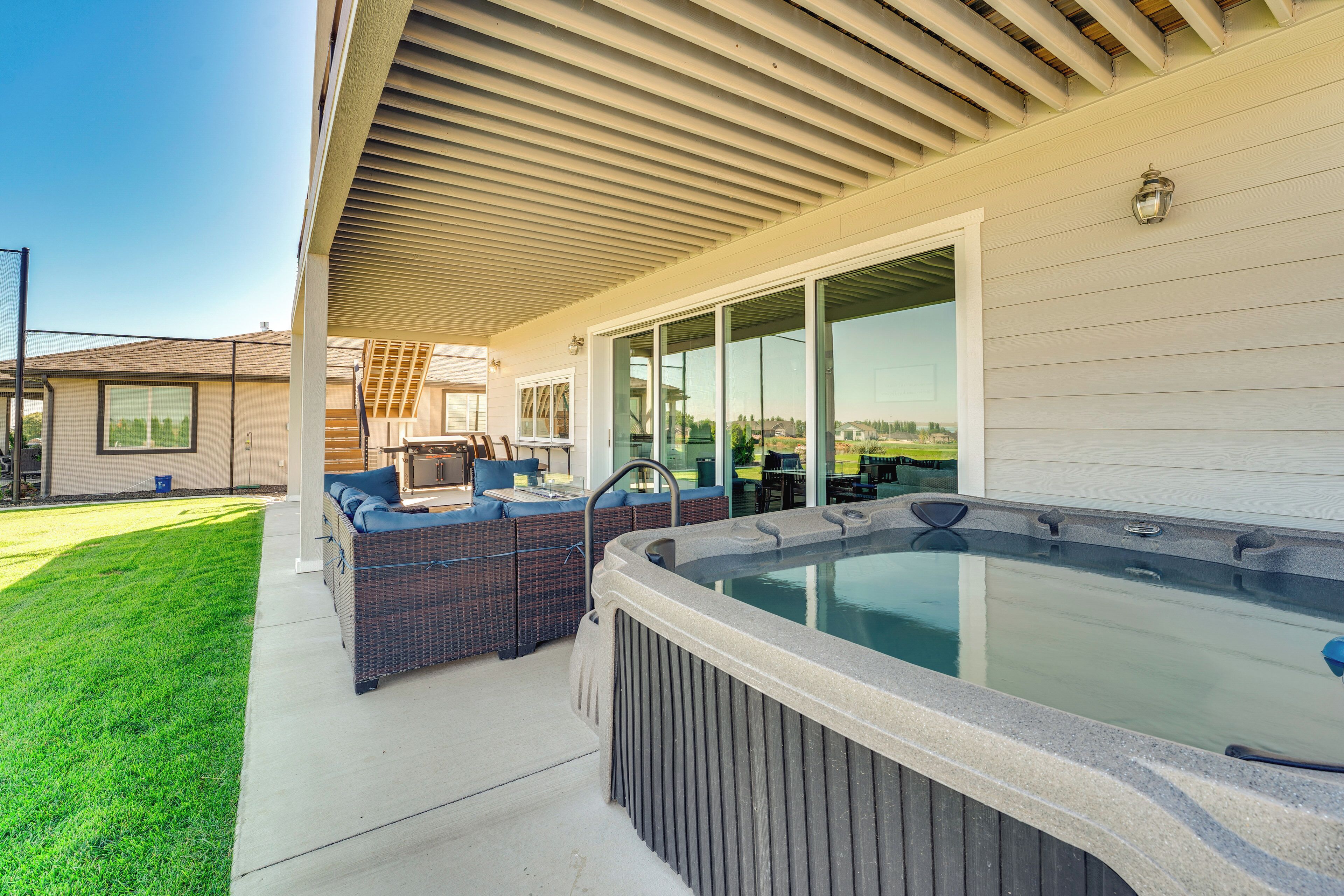An outdoor patio with a hot tub, wicker furniture, and a covered seating area.