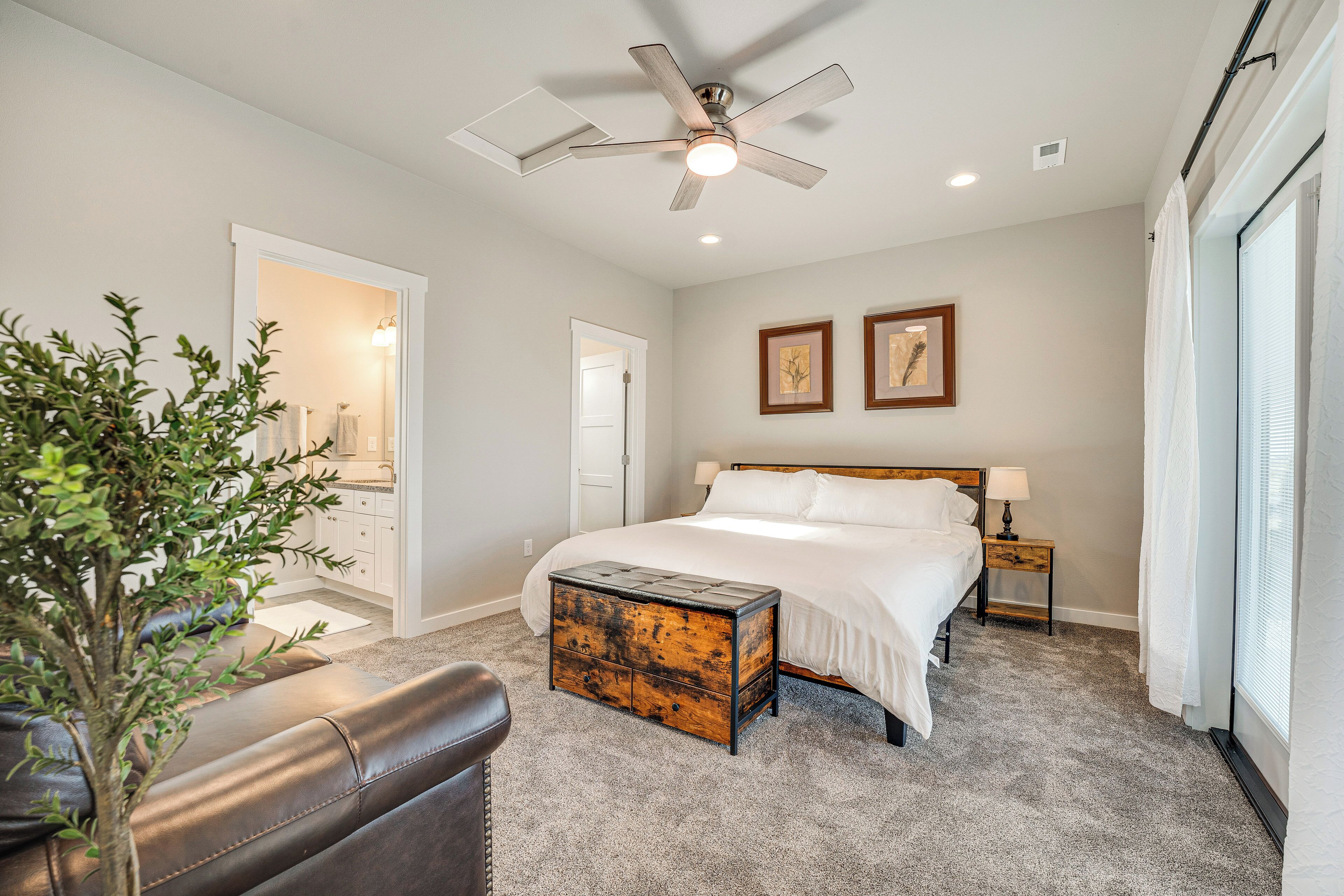 A bedroom with a bed, bedside tables, a ceiling fan, and a large window with blinds.