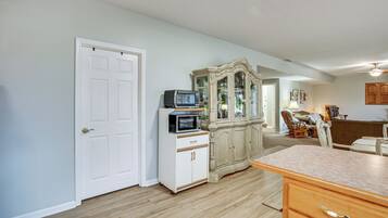 A room with a white door, a microwave on a white cabinet, a wooden cabinet with glass doors, and a wooden counter.