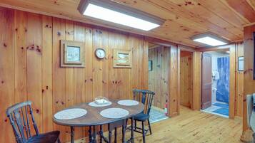 A wooden-paneled room with a round table and four chairs, a clock, and framed pictures on the walls.