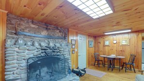 A stone fireplace with a welcome sign, wooden walls, a dining table with chairs, and a cozy seating area. - Dog-friendly Burnsville Cabin Rental Near Hiking! (Burnsville)