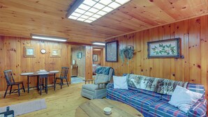 A wooden-paneled room with a plaid sofa, a round table, and a chair. - Dog-friendly Burnsville Cabin Rental Near Hiking! (Burnsville)
