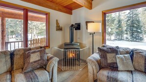 A cozy living room with a fireplace, wooden beams, and large windows with a snowy view. - Peaceful Donnelly Retreat < 1 Mi to Lake Cascade! (Donnelly)