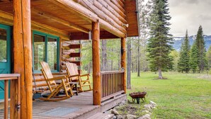A log cabin with a wooden porch, rocking chairs, and a wheelbarrow. - Peaceful Donnelly Retreat < 1 Mi to Lake Cascade! (Donnelly)