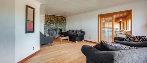 A spacious living room with a stone fireplace, a wooden coffee table, and two dark grey sofas.