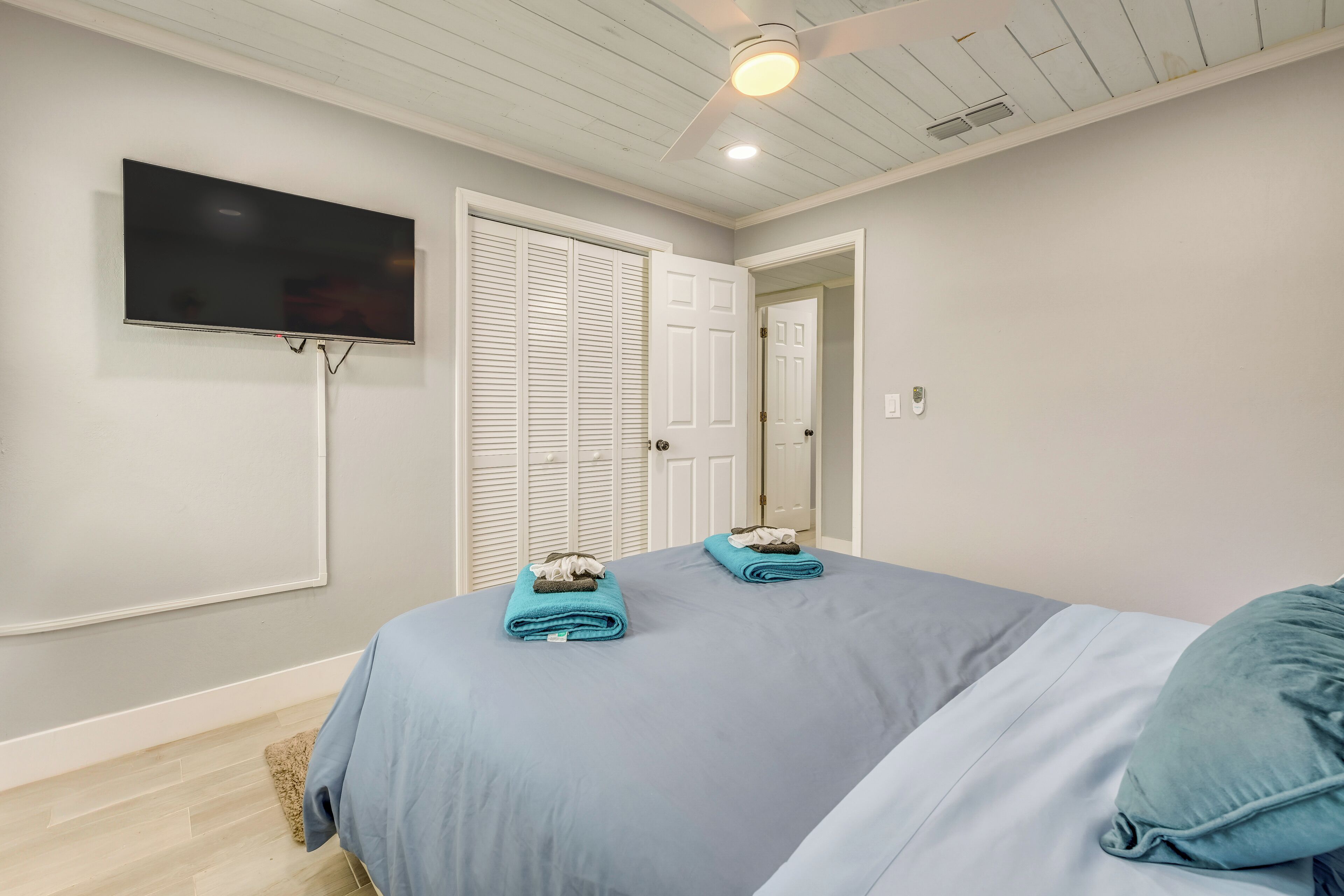 A bedroom with a bed, a TV mounted on the wall, and a ceiling fan.