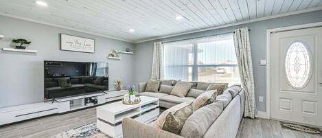 A modern living room with a sectional sofa, a flat-screen TV, and a decorative wall piece.