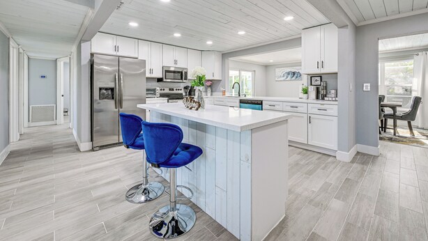 A modern kitchen with white cabinets, stainless steel appliances, and a central island with blue bar stools. - Pool + Screened Lanai! Florida Gulf Coast Getaway (Rotonda West)