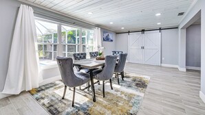 A dining area with a wooden ceiling, large windows with white curtains, a grey upholstered table, and matching chairs. - Pool + Screened Lanai! Florida Gulf Coast Getaway (Rotonda West)