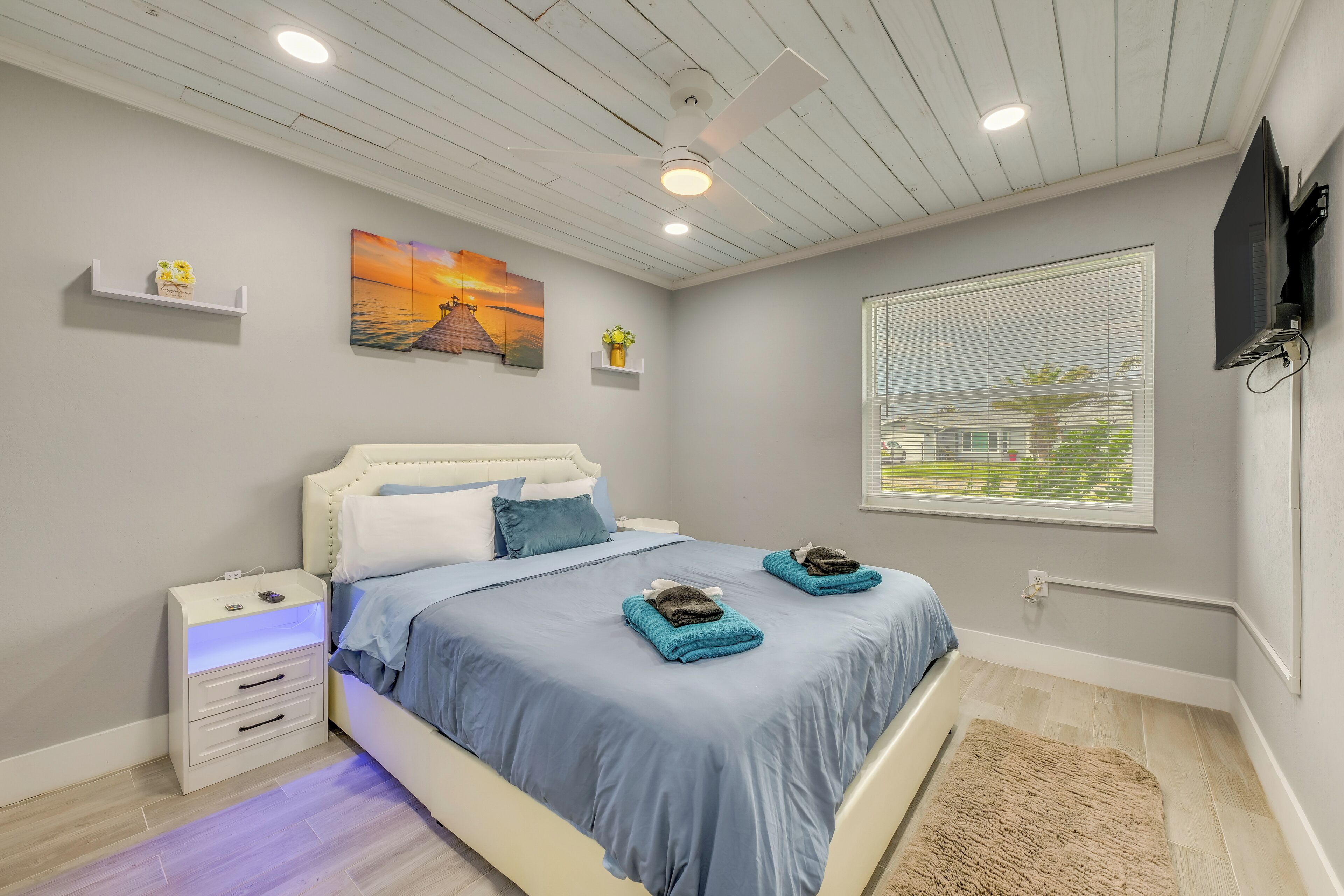 A bedroom with a bed, nightstands, a ceiling fan, a TV, and artwork on the wall.