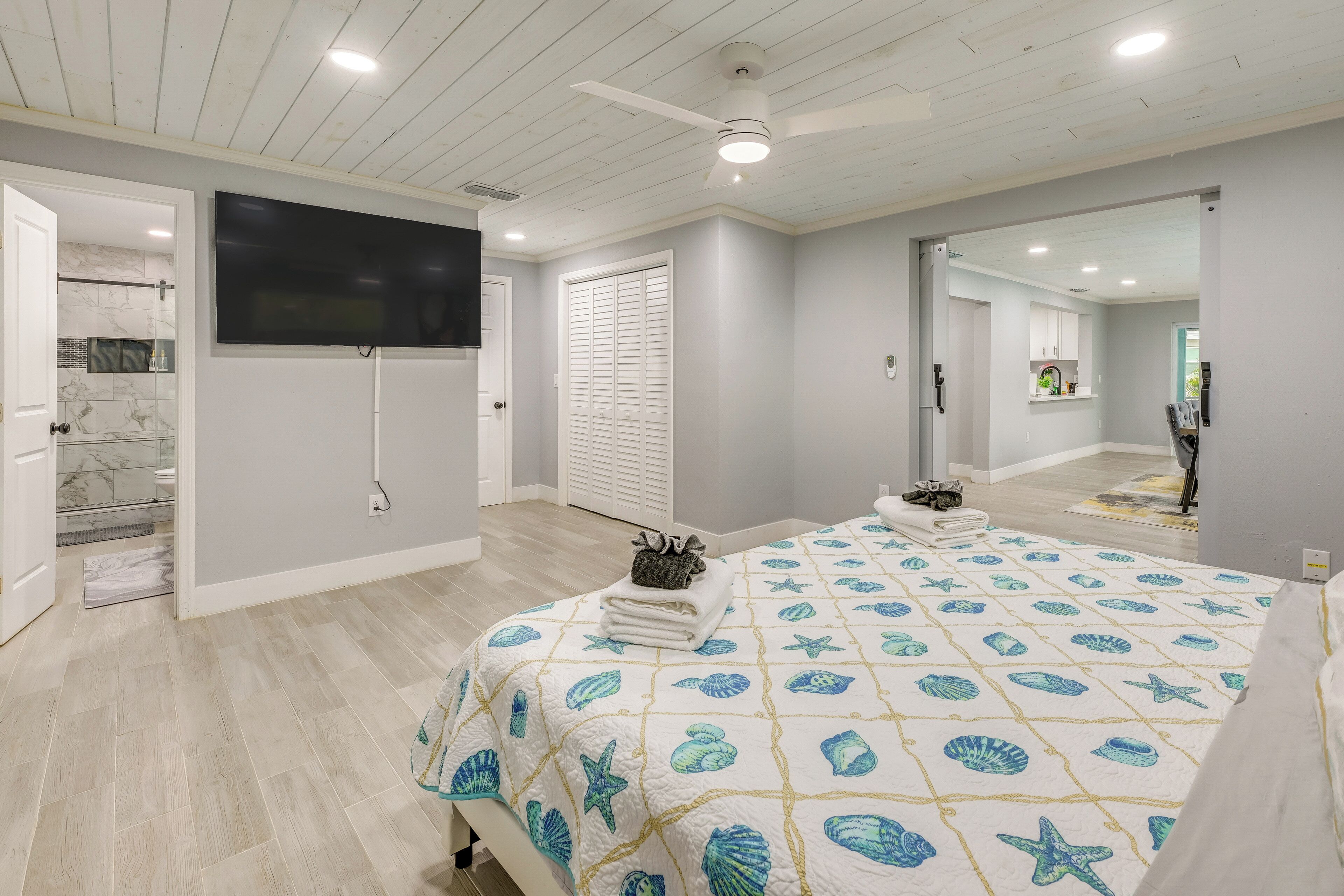 A bedroom with a bed, a ceiling fan, a TV, and a bathroom visible through an open door.