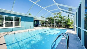 A covered swimming pool with a glass ceiling, surrounded by palm trees and a blue building. - Pool + Screened Lanai! Florida Gulf Coast Getaway (Rotonda West)