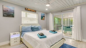 A bedroom with a bed, a nightstand, and a view of the outdoors through a sliding glass door. - Pool + Screened Lanai! Florida Gulf Coast Getaway (Rotonda West)