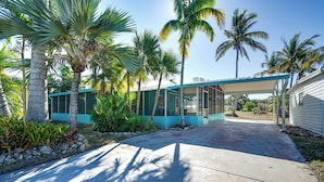 Une maison moderne dotée d’un patio couvert, entourée de palmiers et de plantes tropicales.