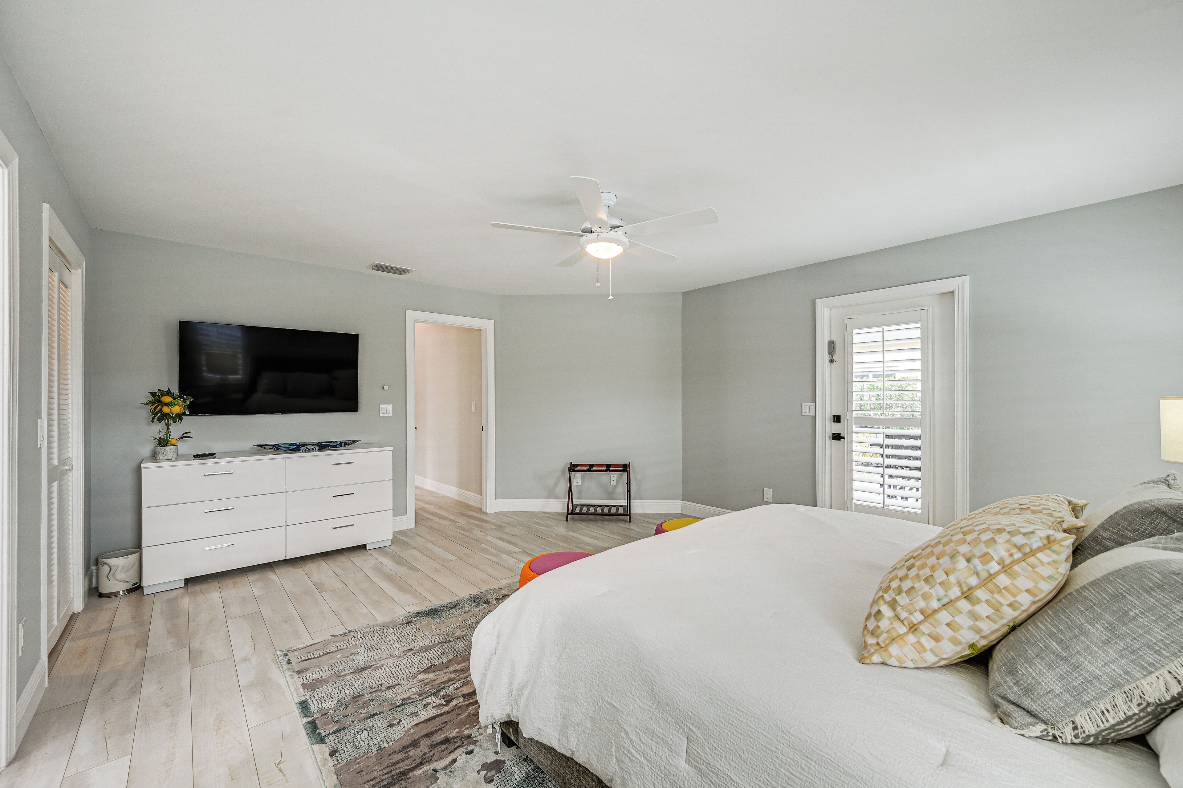 A bedroom with a bed, a TV, a ceiling fan, and a dresser.