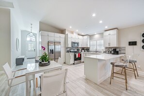 Una cocina moderna con armarios blancos, una isla central y un comedor con mesa y sillas.