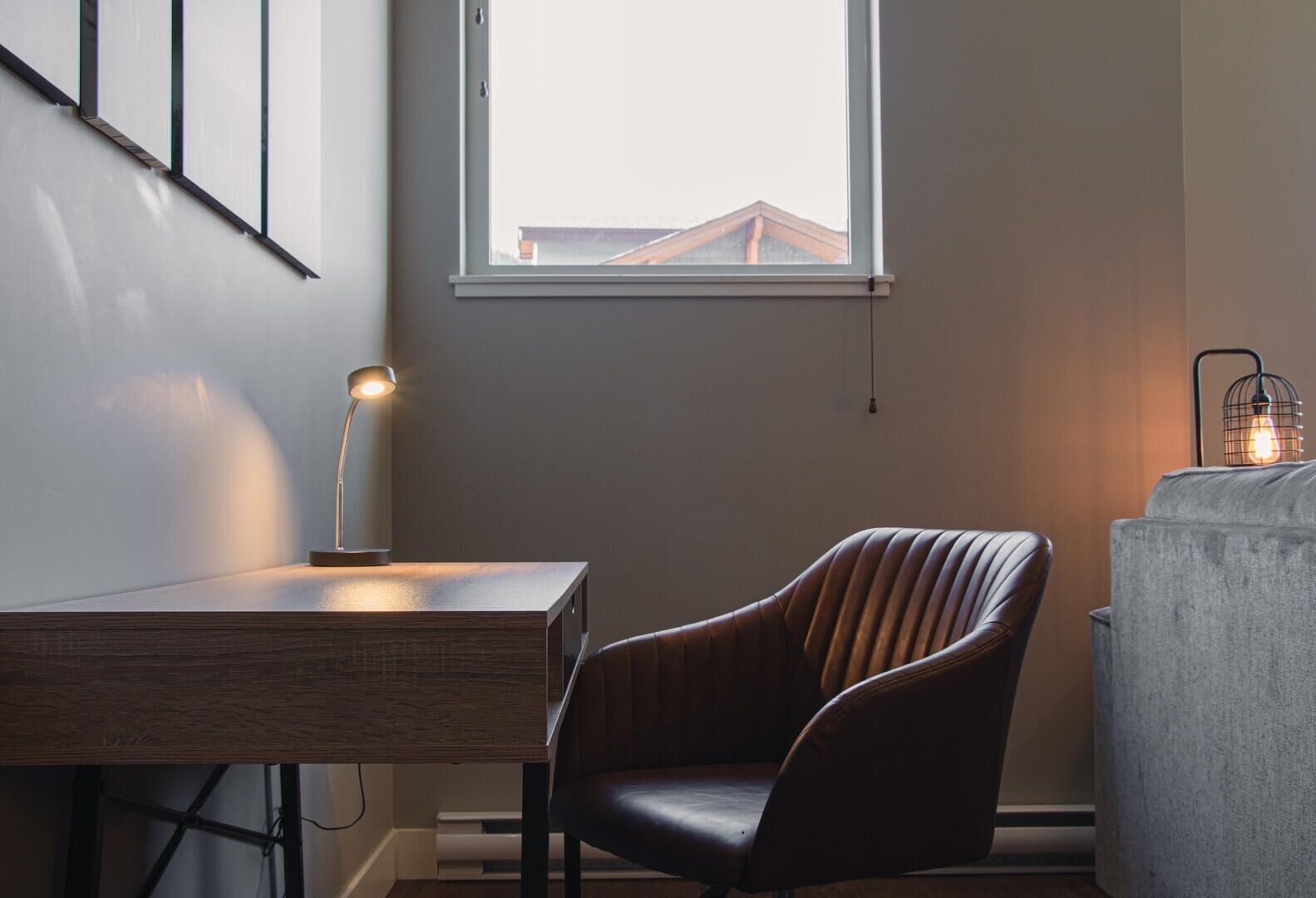 A modern room with a desk, a leather chair, a window, and a lamp.