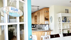 Una cocina con armarios de madera, encimera blanca y comedor con mesa y sillas blancas.