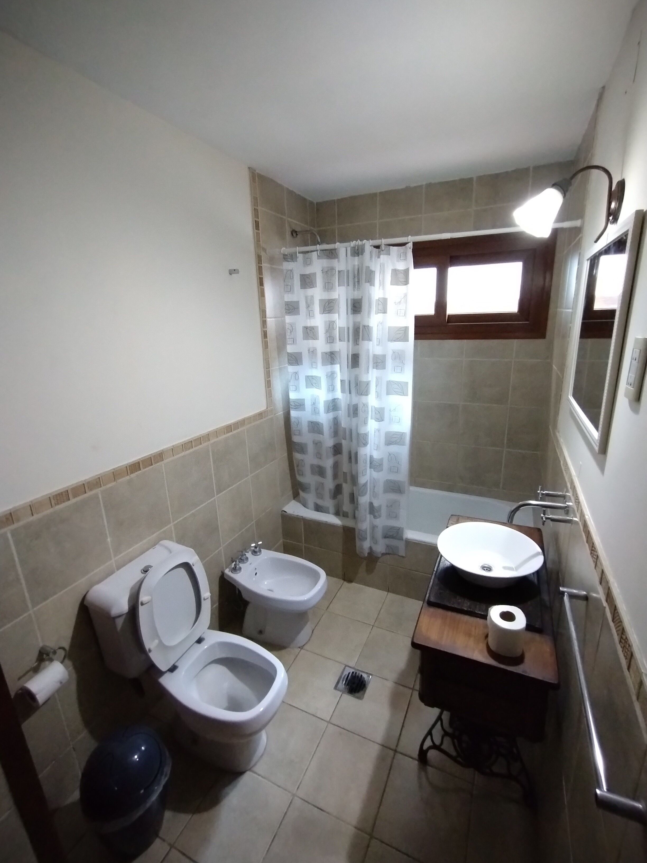A bathroom with two toilets, a bidet, a sink, a shower curtain, and a window.