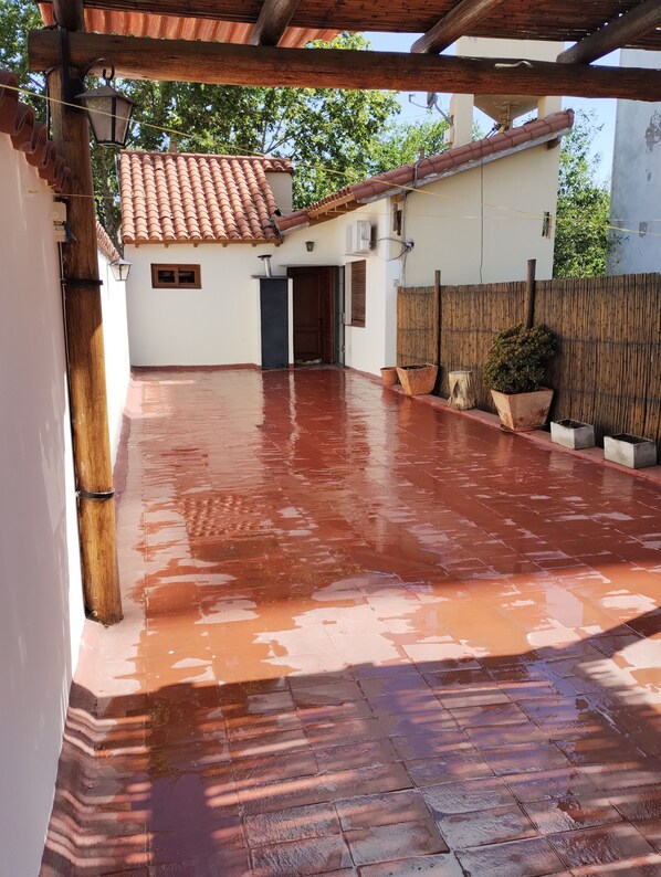 Un patio cubierto con suelo de baldosas, una pérgola de madera y un edificio blanco con tejado de tejas.