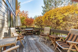 A wooden deck with outdoor furniture, including chairs and a table, and a view of trees with autumn foliage.