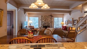 A dining area with a wooden table, chairs, and a kitchen counter in the foreground. There is a stone wall with a fireplace in the background. - Dollar Meadows Condo 1362- Room for the Whole Family at Sun Valley Resort! (Sun Valley)