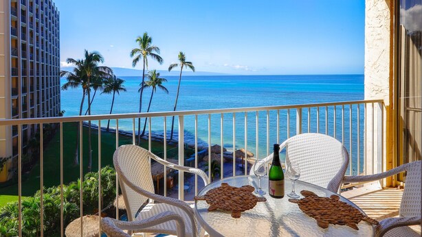 A balcony with wicker chairs, a table, and a bottle of wine.
