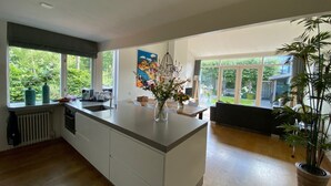 Eine moderne Küche mit einer großen Kochinsel, einem Essbereich mit einer Bank und Blick auf den Garten durch große Fenster.