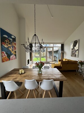 Un comedor con mesa de madera, sillas blancas, una araña y obras de arte en las paredes.
