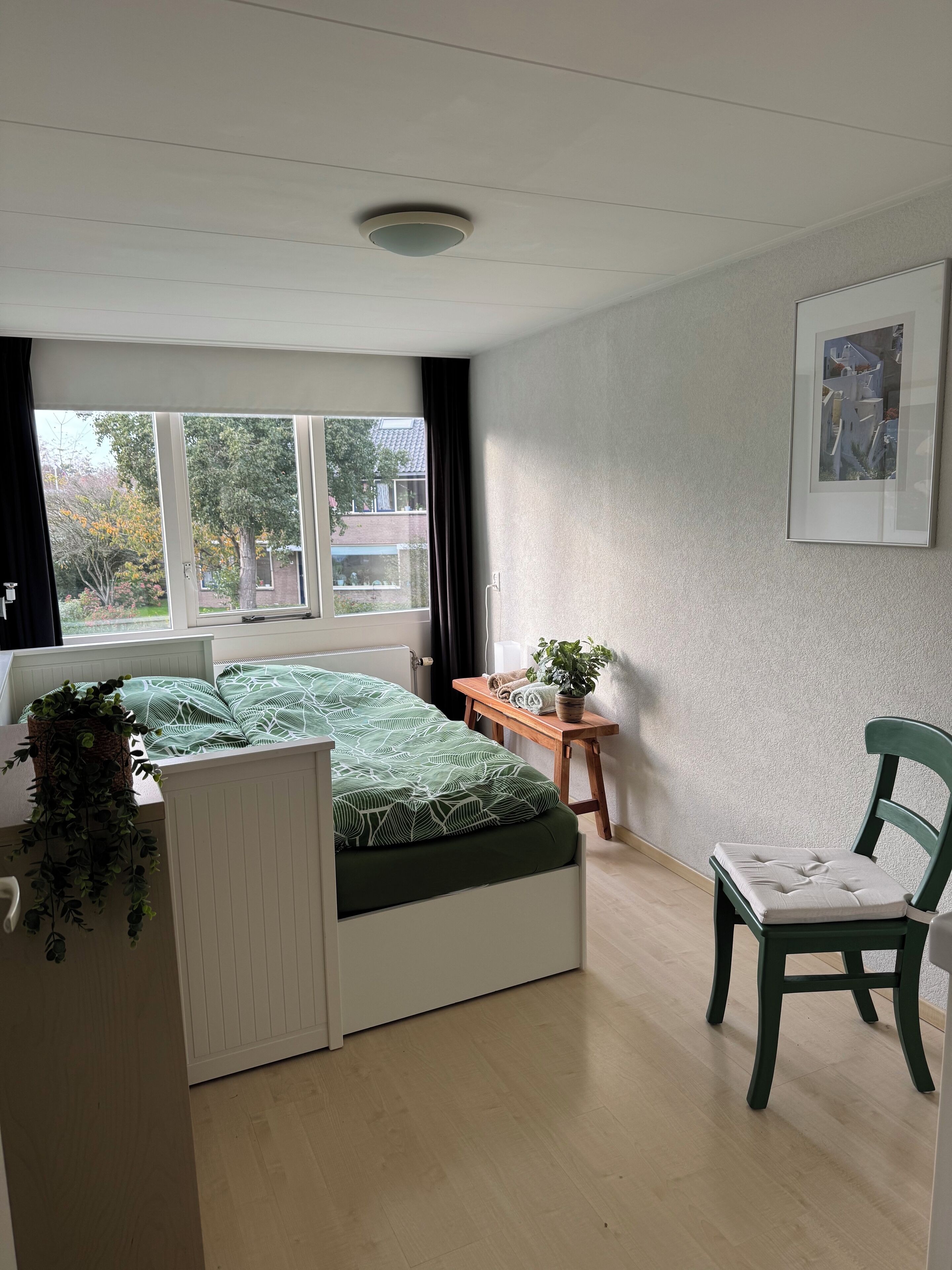Ein Schlafzimmer mit Bett, Schreibtisch, Stuhl, Fenster und Deckenleuchte.