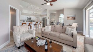 A spacious living room with a sofa, chairs, a coffee table with wine glasses, and a ceiling fan.
