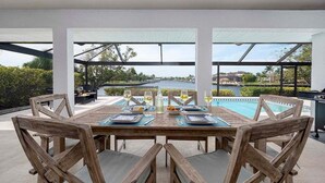 An outdoor dining area with a view of a lake and hills, wooden furniture, and a pool in the background.