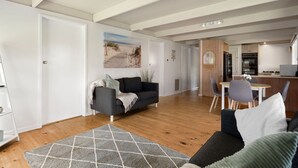 A modern living room with a sofa, a dining table with chairs, and a kitchen area. - Charming Dromana Cottage (Dromana)