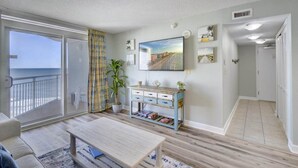 A living room with a large window, a sofa, a coffee table, a TV, and a blue cabinet. - HS-1129 Spacious 2-bedroom condo in Myrtle Beach (Myrtle Beach)