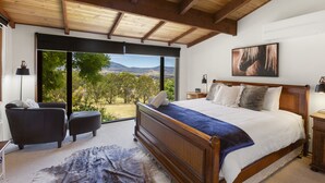 Ein Schlafzimmer mit einem großen Bett, Blick ins Freie, Holzboden und einem Gemälde an der Wand.