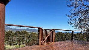 Eine Holzterrasse mit einem Metalltor, mit Blick auf eine Landschaft mit Bäumen und fernen Bergen.