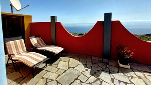 Una terrazza con due poltrone a righe, una pianta in vaso e vista sull'oceano.