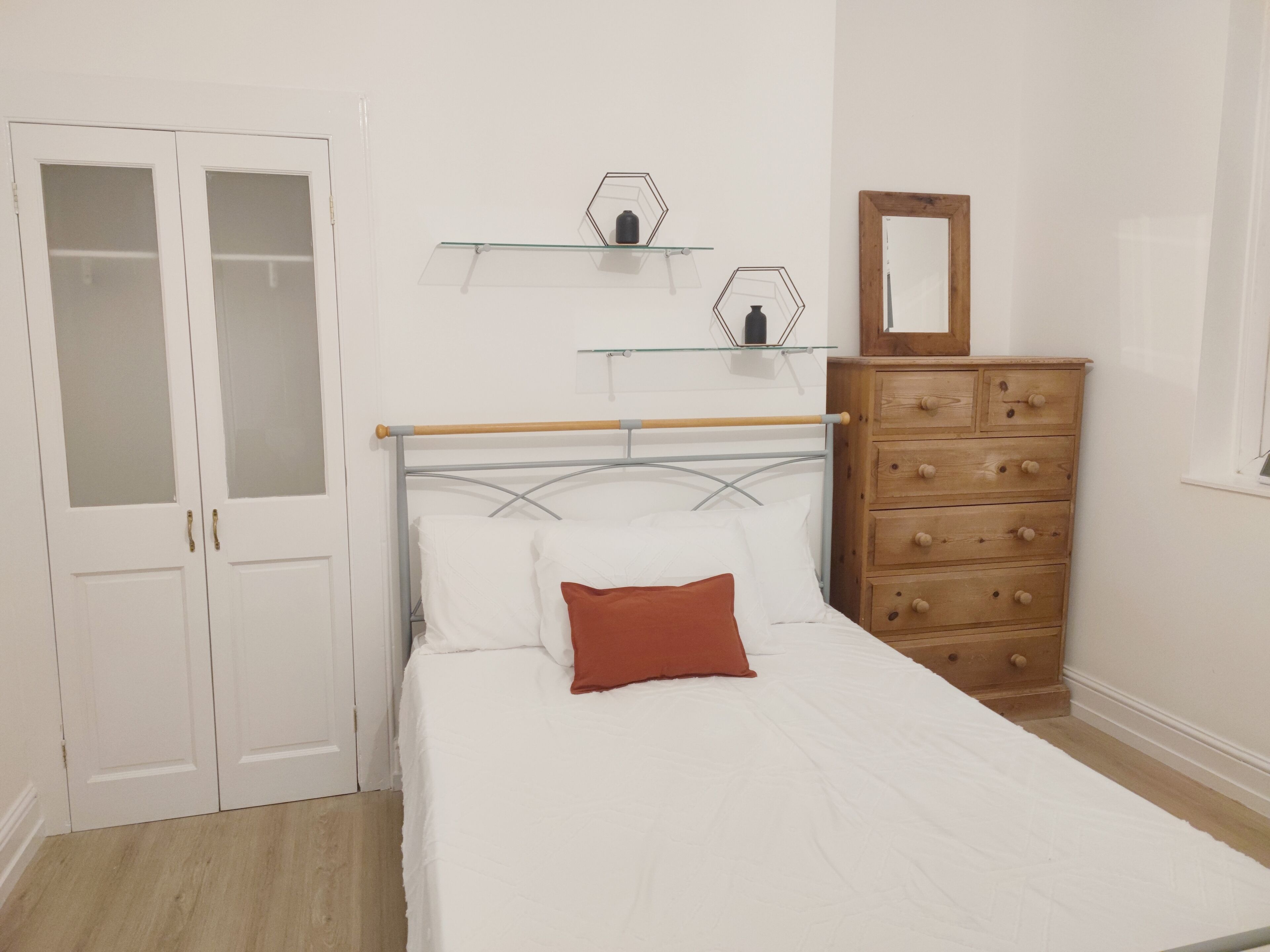 A bedroom with a bed, a dresser, and two glass-fronted shelves.