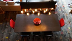 A dining table with a central red spiral object, surrounded by four red chairs, under a string of exposed bulbs. - Ferme du Cugnon (Les Contamines-Montjoie)