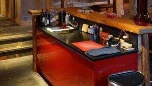 A rustic interior with exposed wooden beams, a bar area with stools, and a framed picture on the wall. - Ferme du Cugnon (Les Contamines-Montjoie)