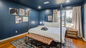 A bedroom with a four-poster bed, a bench, and a nightstand with a lamp. - 4-BD Mid-Modern Century with Firepit & Playground (Houston)