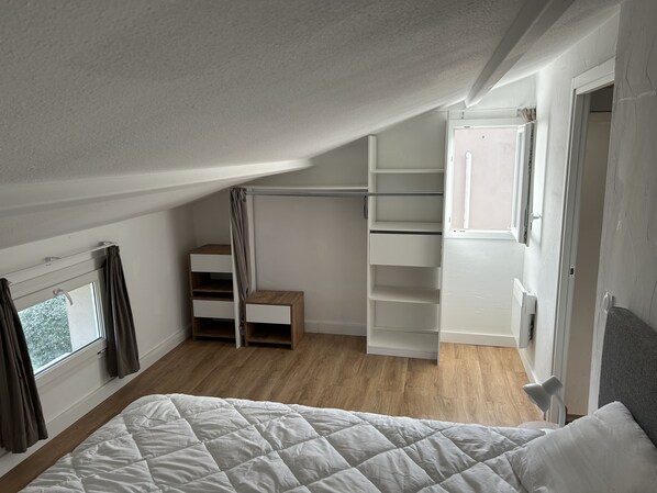 A bedroom with a bed, a wooden floor, a closet with shelves, and a window.