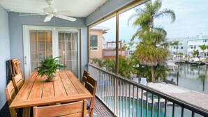 Une table en bois, entourée de chaises, sur un balcon donnant sur une piscine et un port de plaisance.