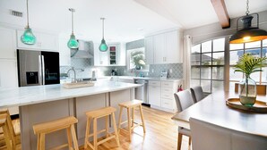 Une cuisine moderne avec des meubles blancs, un grand îlot central doté de tabourets et un éclairage suspendu.