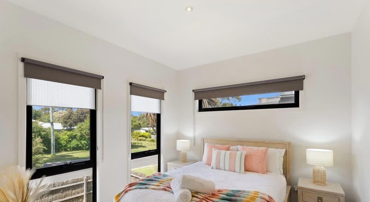 A bedroom with a bed, two bedside tables, a window with a view of greenery, and a ceiling light.