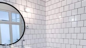 Une salle de bain moderne avec des carreaux de métro blancs, un miroir rond, un meuble-lavabo en bois, une baignoire et un tabouret en osier.