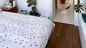 Une chambre à coucher avec un lit, une table de chevet, une plante en pot et une porte donnant sur une autre pièce.
